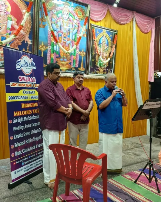 Man speaking with microphone at temple event with Swaram banner