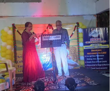 Man and woman singing on stage at live event with banner
