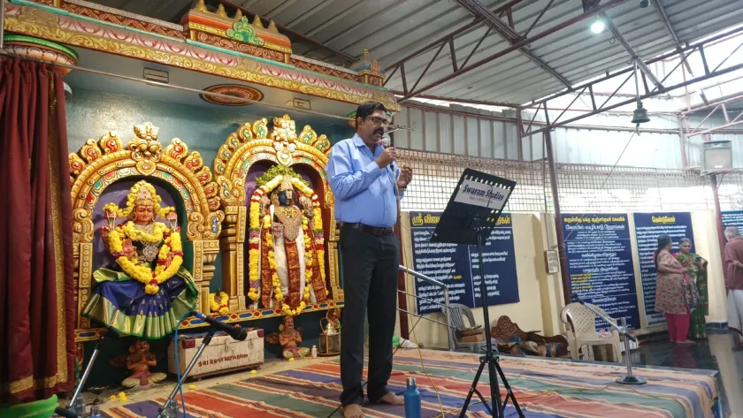 Man speaking at temple stage with decorated deities