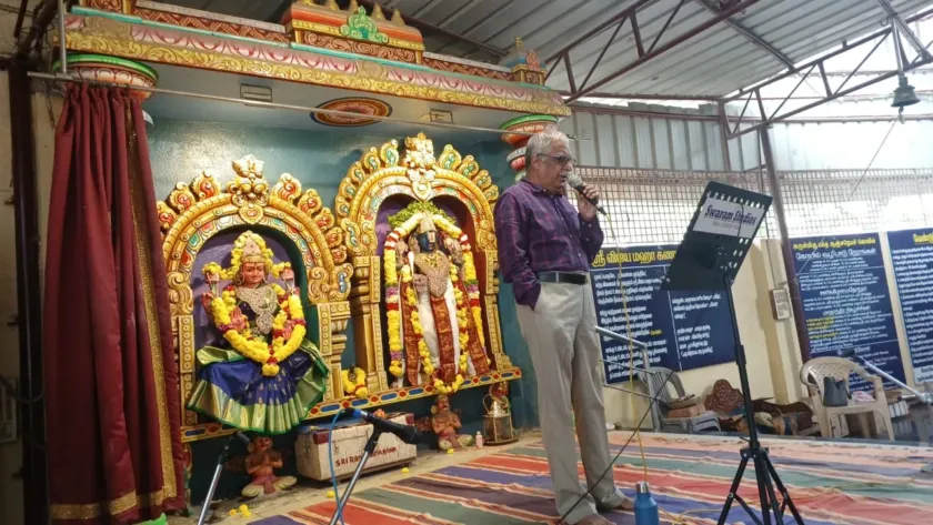 Man speaking at temple stage with decorated deities