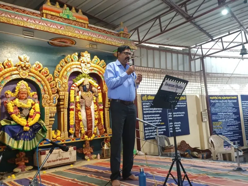 Man speaking at temple event with decorated deities Image